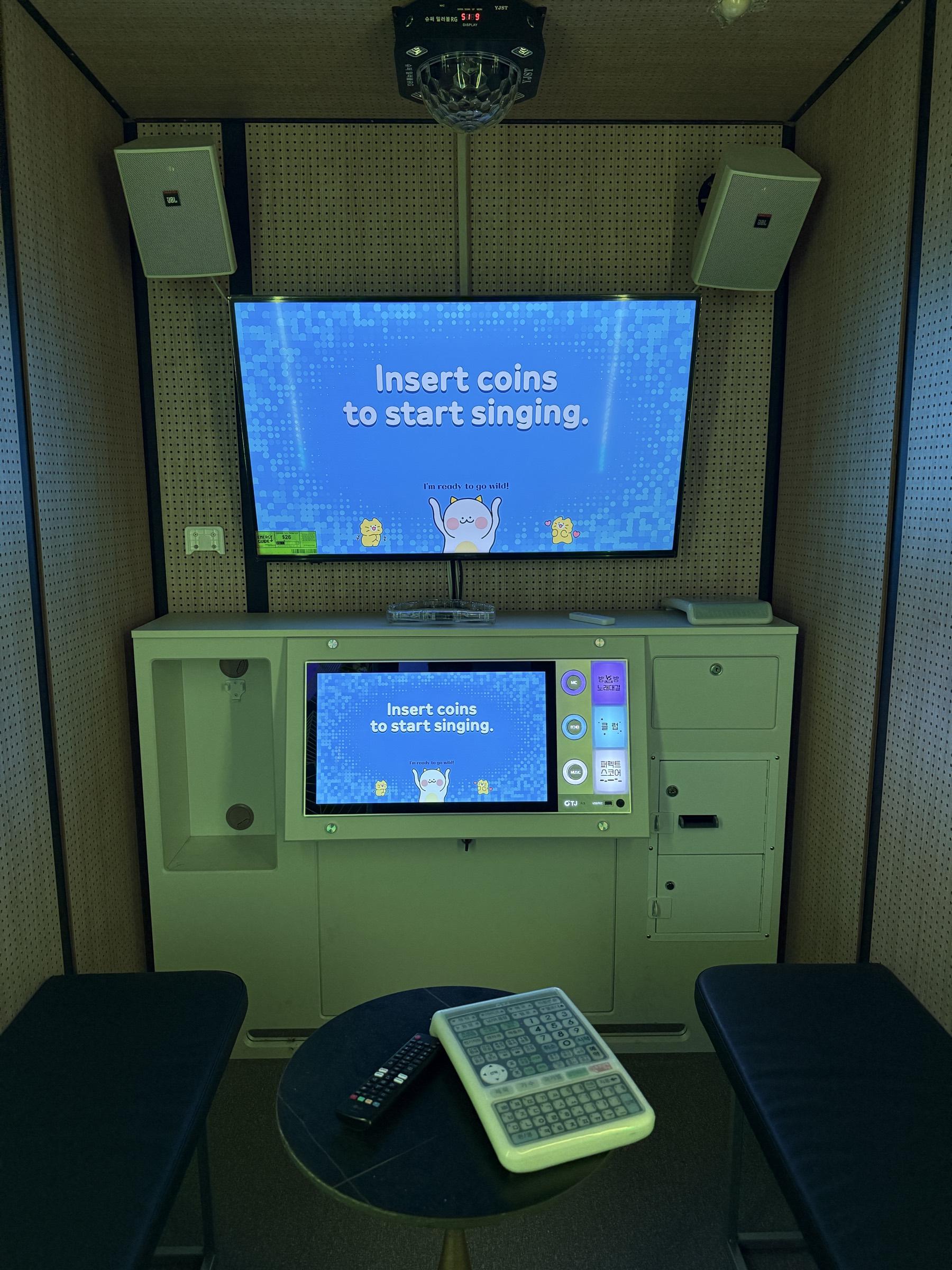 A private karaoke room lit in purple, with its own screen and speakers above bench seating and a low table.